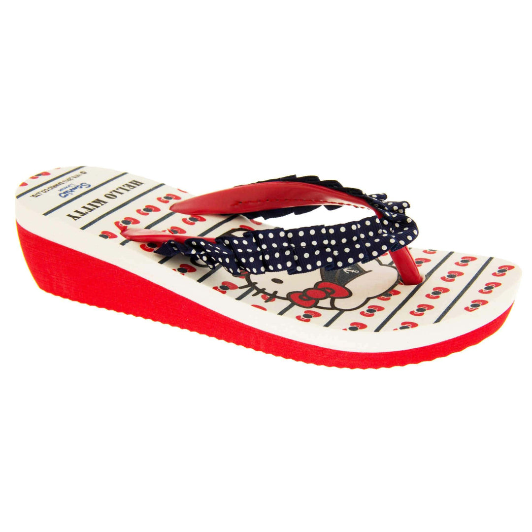 Girls wedge sandals. Hello Kitty flip flop sandal. White top with Hello Kitty design. Red synthetic between toe strap with blue textile frill with white spots. Small wedge heel. Red sole. Right foot at an angle