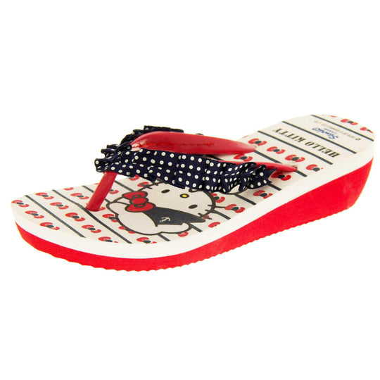 Girls wedge sandals. Hello Kitty flip flop sandal. White top with Hello Kitty design. Red synthetic between toe strap with blue textile frill with white spots. Small wedge heel. Red sole. Left foot at an angle
