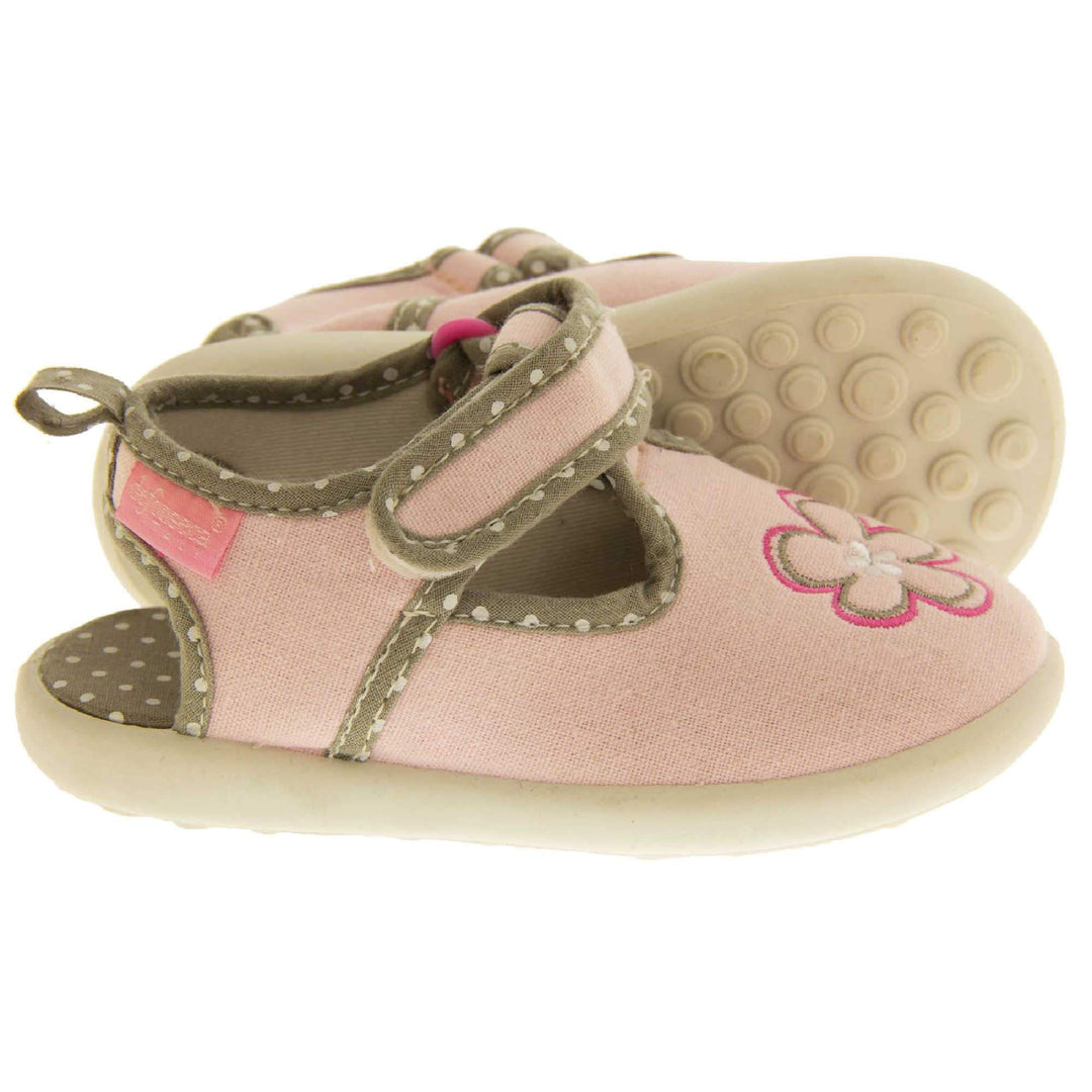 Girls sandals. Pink canvas t-bar pumps with white sole, flower detail to the front and brown edging with white dots. Cut out heel visible with matching brown insoles with white dots. Both feet from side angle but with left foot on its side so you can see the sole.