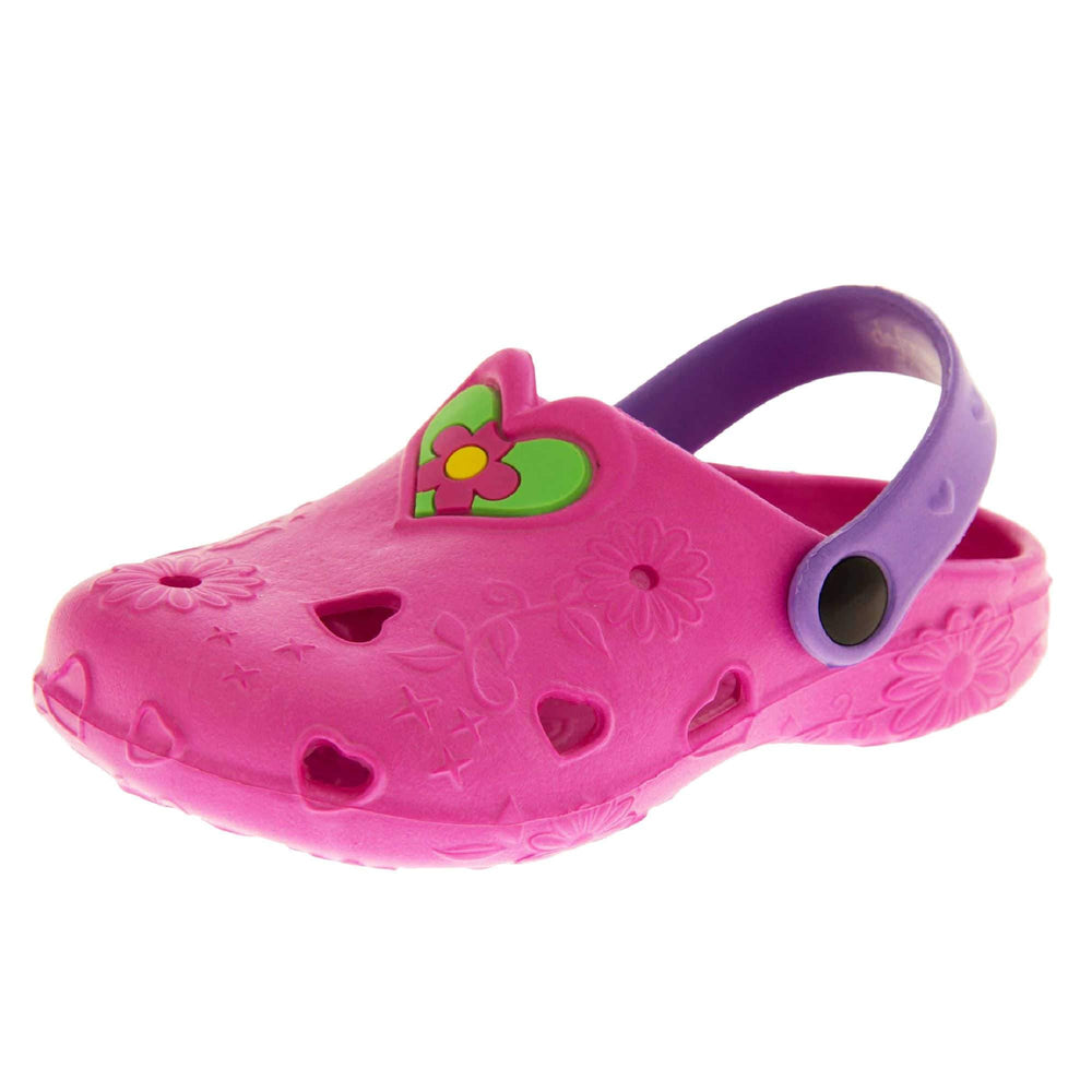 Girls Sandals. Pink synthetic clog style shoes with embossed flowers and stars. Cut out love hearts on the upper. Green love heart, with pink and yellow flower in the centre, to the middle top of the upper. Purple strap that goes along the back of your heel. The strap can be moved along the top of the shoe instead to make the shoe a mule. Left foot at an angle
