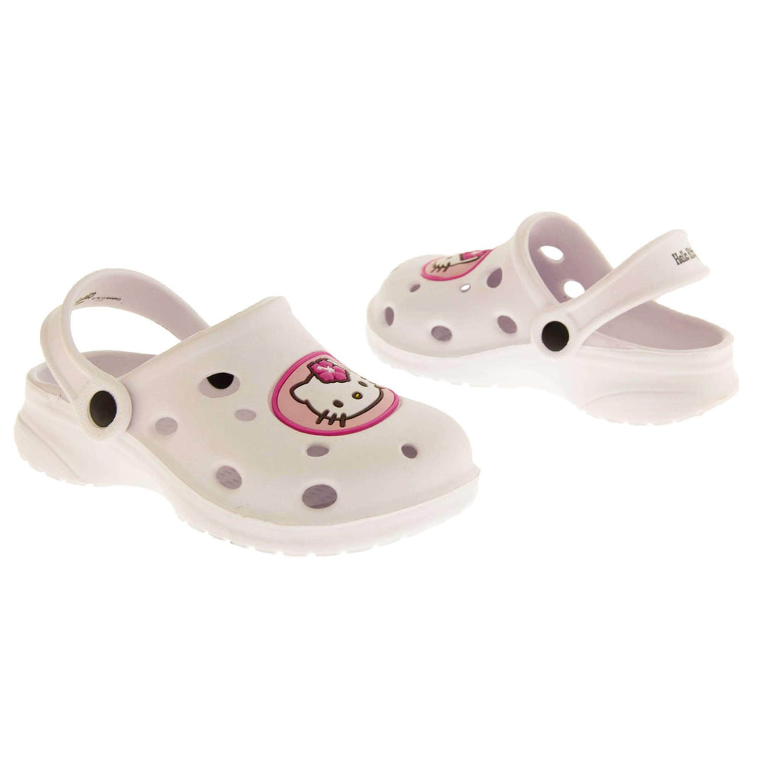 Girls Sandals White. White synthetic clog sandals with holes in the upper. Hello Kitty face in a pink circle to the front. White strap with black studs to attach to the back of the shoe. The strap can be worn around the back of the heel or over the top of the shoe in a mule. White sole with slight heel to the back. Both shoes facing top to tail and from an angle.