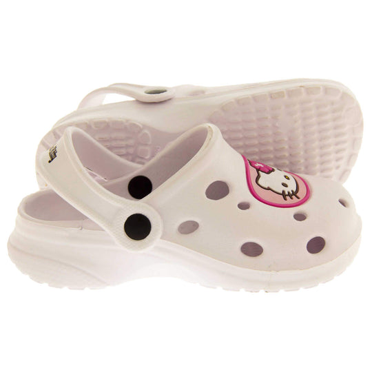 Girls Sandals White. White synthetic clog sandals with holes in the upper. Hello Kitty face in a pink circle to the front. White strap with black studs to attach to the back of the shoe. The strap can be worn around the back of the heel or over the top of the shoe in a mule. White sole with slight heel to the back. Both feet from a side profile with the left foot on its side to show the sole.