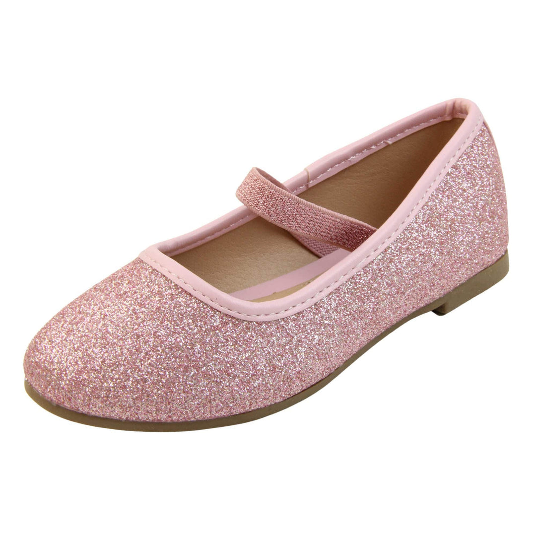 Girls sparkly shoes. Ballerina style shoes with pink glitter uppers. With a pink glitter elasticated over the foot strap. Pink faux leather collar and beige lining. Dark brown sole with very slight heel. Left foot at an angle.