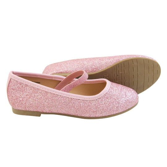 Girls sparkly shoes. Ballerina style shoes with pink glitter uppers. With a pink glitter elasticated over the foot strap. Pink faux leather collar and beige lining. Dark brown sole with very slight heel. Both feet from a side profile with the left foot on its side behind the the right foot to show the sole.