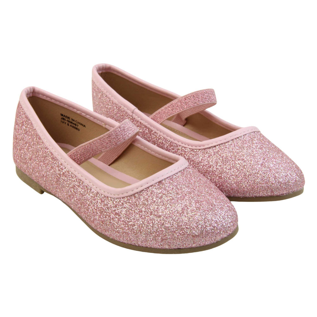 Girls sparkly shoes. Ballerina style shoes with pink glitter uppers. With a pink glitter elasticated over the foot strap. Pink faux leather collar and beige lining. Dark brown sole with very slight heel. Both feet together at an angle.