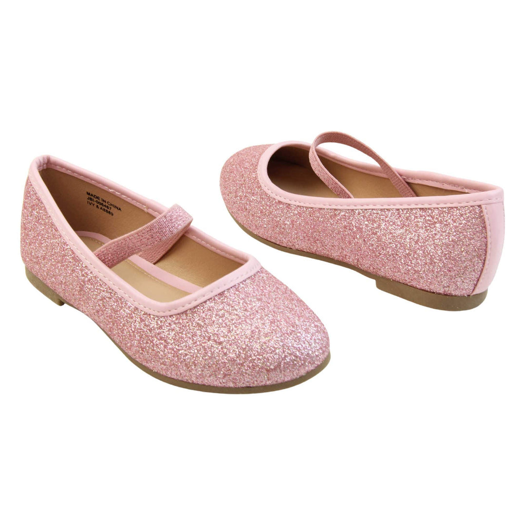 Girls sparkly shoes. Ballerina style shoes with pink glitter uppers. With a pink glitter elasticated over the foot strap. Pink faux leather collar and beige lining. Dark brown sole with very slight heel. Both feet at an angle facing top to tail.