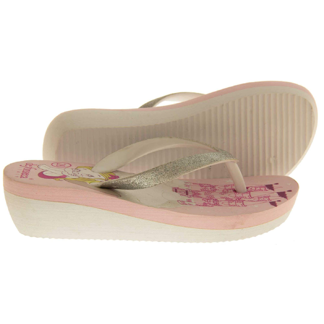 Foam wedge sandals for girls. White bottom half of the sole with ridges for grip, baby pink top half with bright pink fantasy design to the insole. White strap with toe post covered on top with pale gold glitter. Both feet from side profile with left foot on its side to show the sole.
