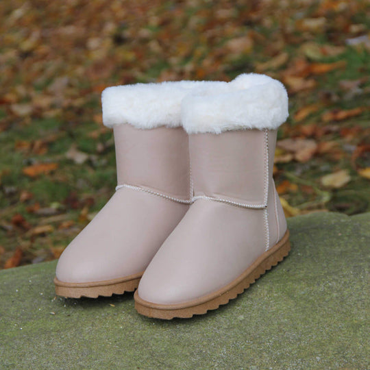 Girls Winter Boots - Beige glitter shimmer boots with visible stitching detail, white faux fur collar and brown chunky resilient sole. Life style photo. Both boots on a stone in the park.