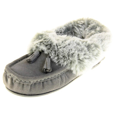 Grey Moccasin Slippers. Womens grey faux suede moccasin style slippers. With stitched detailing and tassels with subtle glitter on. Pale grey faux fur collar and lining. Grey firm sole. Left foot at an angle.