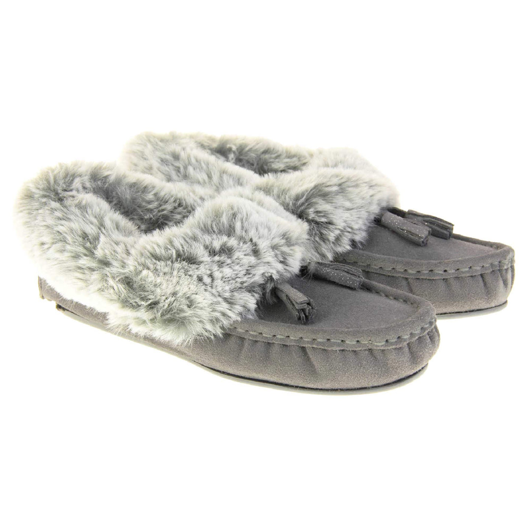 Grey Moccasin Slippers. Womens grey faux suede moccasin style slippers. With stitched detailing and tassels with subtle glitter on. Pale grey faux fur collar and lining. Grey firm sole. Both feet together at an angle.