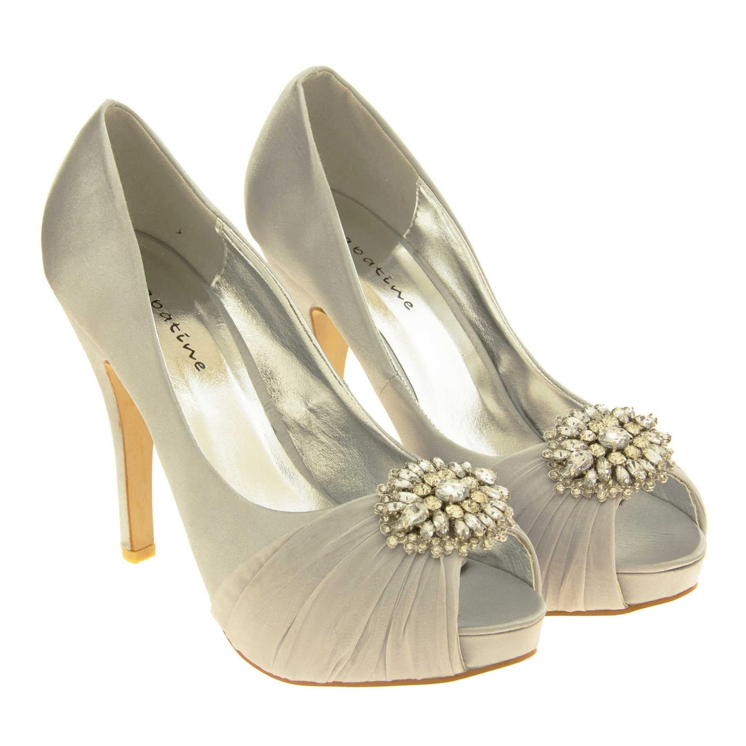 Grey satin heels. Classic women's peep toe high heels with a pale grey satin upper. Metallic silver insole with Sabatine branding. Grey satin stiletto heel with a cream sole. Diamante cluster and ruched detailing across the toes. Both feet together at a slight angle.