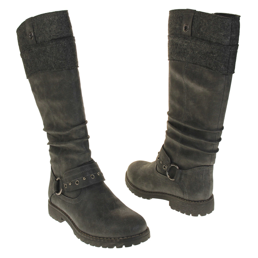 Grey suede boots knee high. Tall boots with a grey faux nubuck leather upper with a felt decorative cuff around the top. A strap with stud embellishment goes around the front of the ankle connected by a silver loop. Stitching detail around the outsole and the ankle. Full length zip to the inside leg. Both feet from a slight angle facing top to tail.