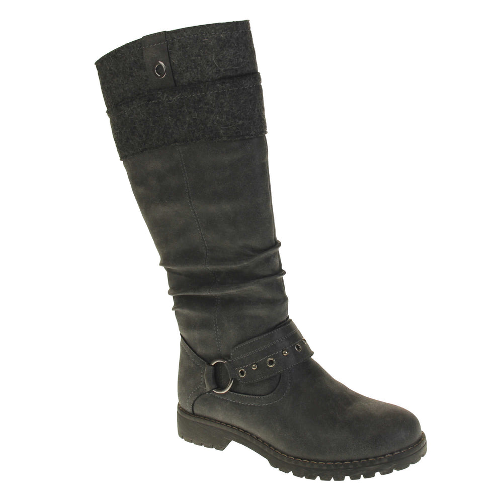 Grey suede boots knee high. Tall boots with a grey faux nubuck leather upper with a felt decorative cuff around the top. A strap with stud embellishment goes around the front of the ankle connected by a silver loop. Stitching detail around the outsole and the ankle. Full length zip to the inside leg. Right foot at an angle.