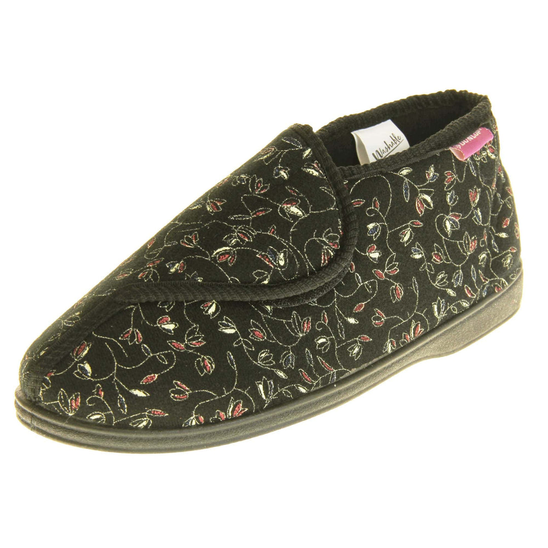 Hard sole slippers womens. Ladies bootie style slipper with a black textile upper with vine flower embroidered design. Touch fasten tab to the top and black textile lining. Firm black sole. Left foot at an angle.