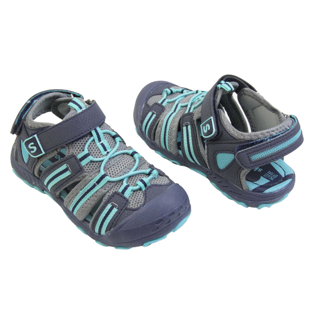 Kids beach sandals. Strappy beach sandals with grey mesh and navy faux leather uppers. with turquoise and navy textile strap detailing. Turquoise elasticated faux laces to the front. Navy faux leather straps around the front and back of the ankle with touch fastening. Turquoise insole. Navy rubbery outsole and toe bumper with turquoise and navy grip on the bottom. Both feet at an angle facing top to tail.