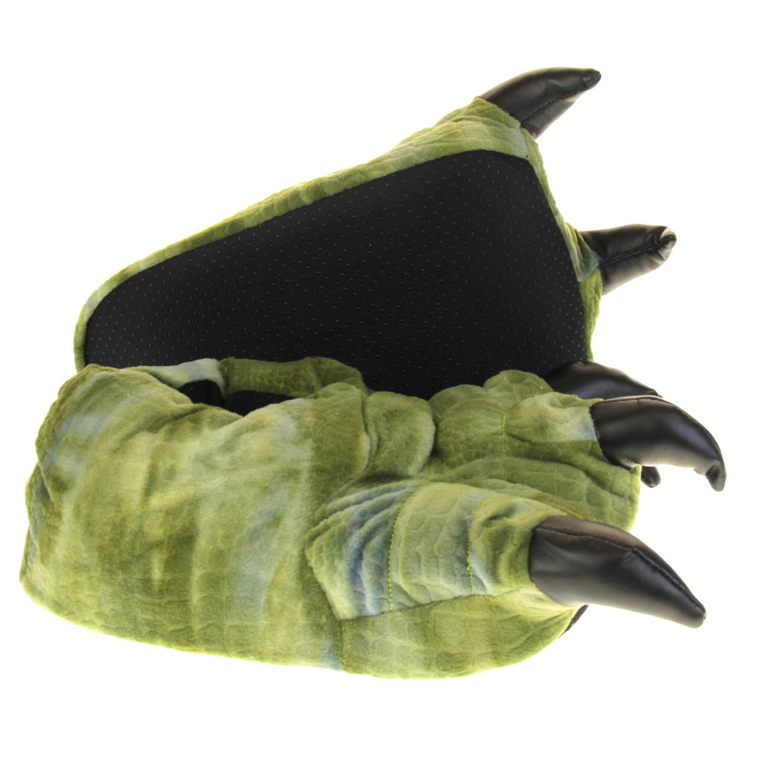 Kids dinosaur slippers. Cushioned slippers shaped like a dinosaur foot. Green textile outer with scale type pattern and black shiny padded claws. Inside is a textile lining. Black soft sole with bumps on for grip. Both feet from side profile with left foot on its side to show the sole.