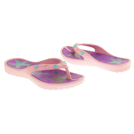 Kids flip flops girls. Pale pink flip flops with toe post strap. Purple insole with glittery heart design on. Small pink and teal plastic stars along the strap. Slip-resistant grip to the sole. Both shoes at an angle facing top to tail.