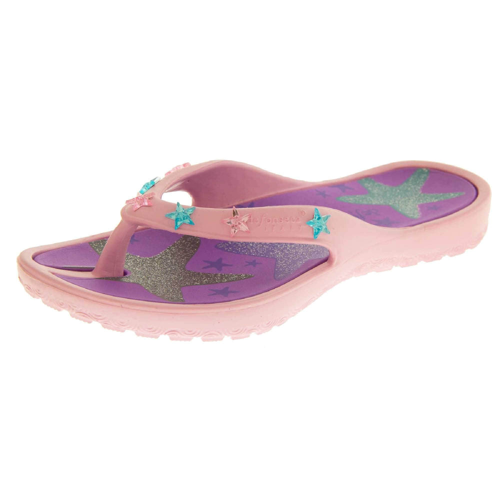 Kids flip flops girls. Pale pink flip flops with toe post strap. Purple insole with glittery star design on. Small pink and teal plastic stars along the strap. Slip-resistant grip to the sole. Left foot view