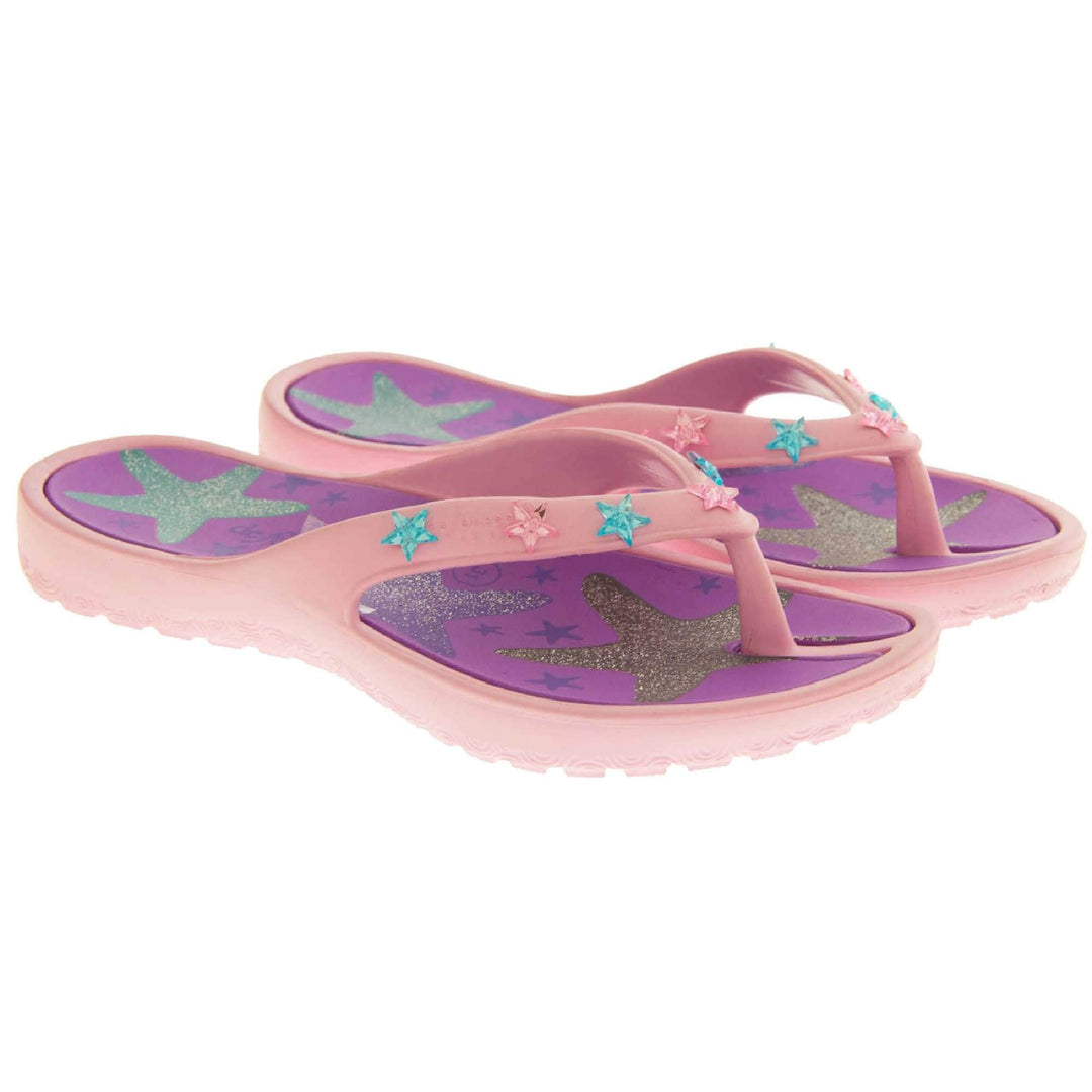 Kids flip flops girls. Pale pink flip flops with toe post strap. Purple insole with glittery heart design on. Small pink and teal plastic stars along the strap. Slip-resistant grip to the sole. Both feet together at an angle.