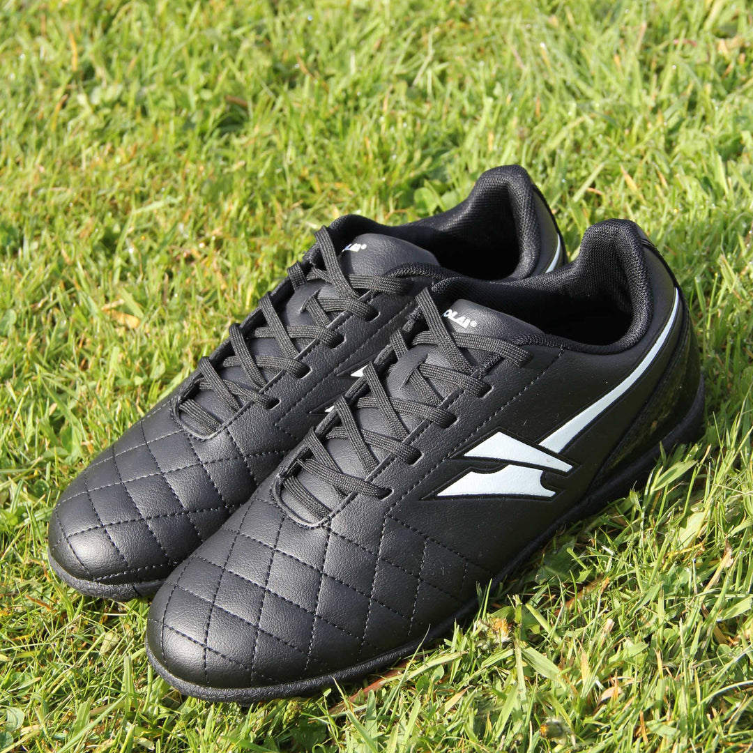 Astro turf boots. Black football trainers with stitching detail to the toes to give a quilted appearance. The black lace fastening to the front. White Gola logo to the side and white Gola branding to the tongue. Black sole with small Astro turf bumps to the base. Lifestyle picture with the boots together on a grass playing field.