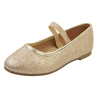Kids glitter shoes. Ballerina style shoes with gold glitter uppers. With a gold glitter elasticated over the foot strap. Gold faux leather collar and beige lining. Dark brown sole with very slight heel. Left foot at an angle.