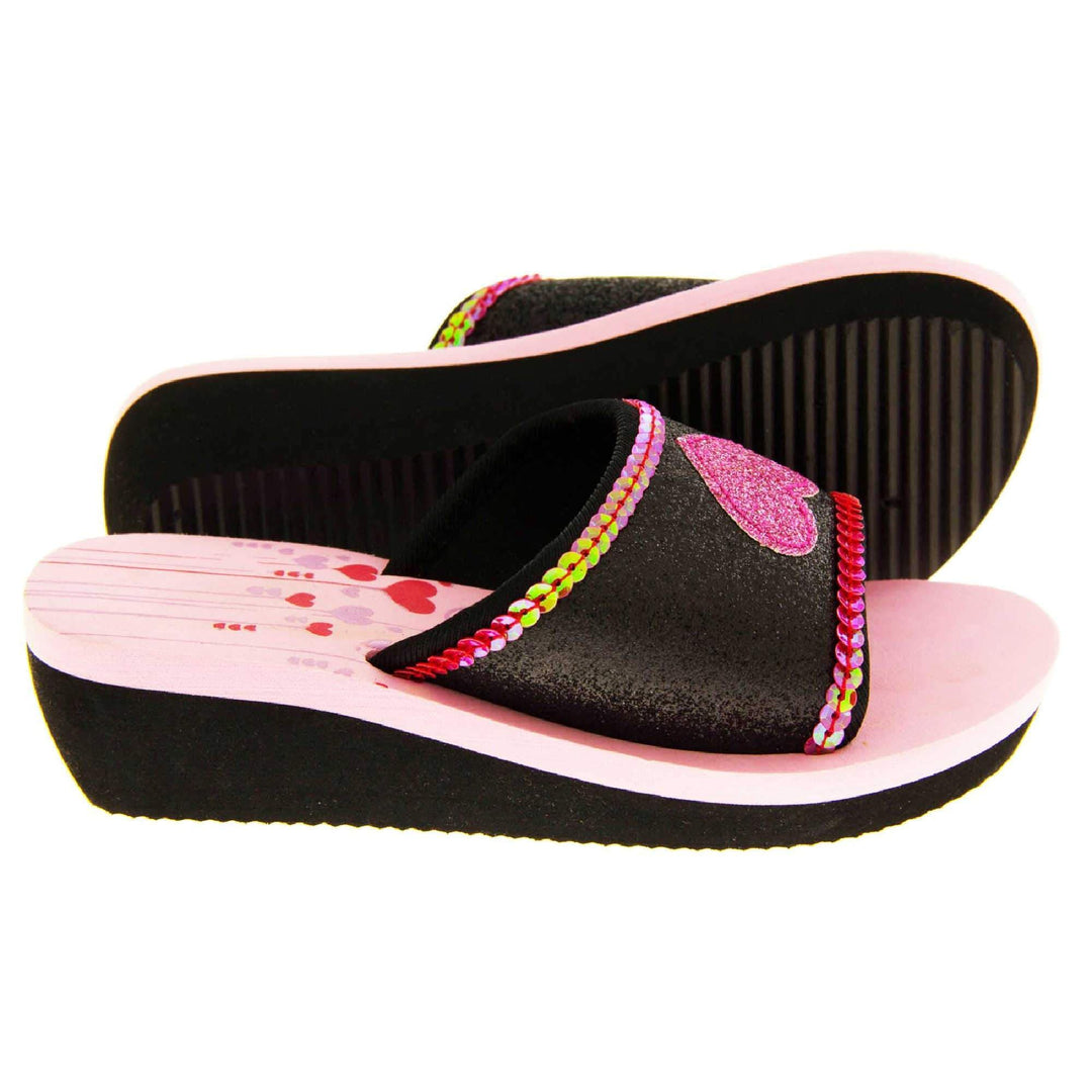 Foam wedge sandals for girls. Black bottom half of the sole with ridges for grip, baby pink top half with red and pale pink heart and line design to the heel of the insole. Black glitter full strap with bright pink glitter heart in the middle and pink sequins along the edges. Both feet from side profile with left foot on its side to show the sole.