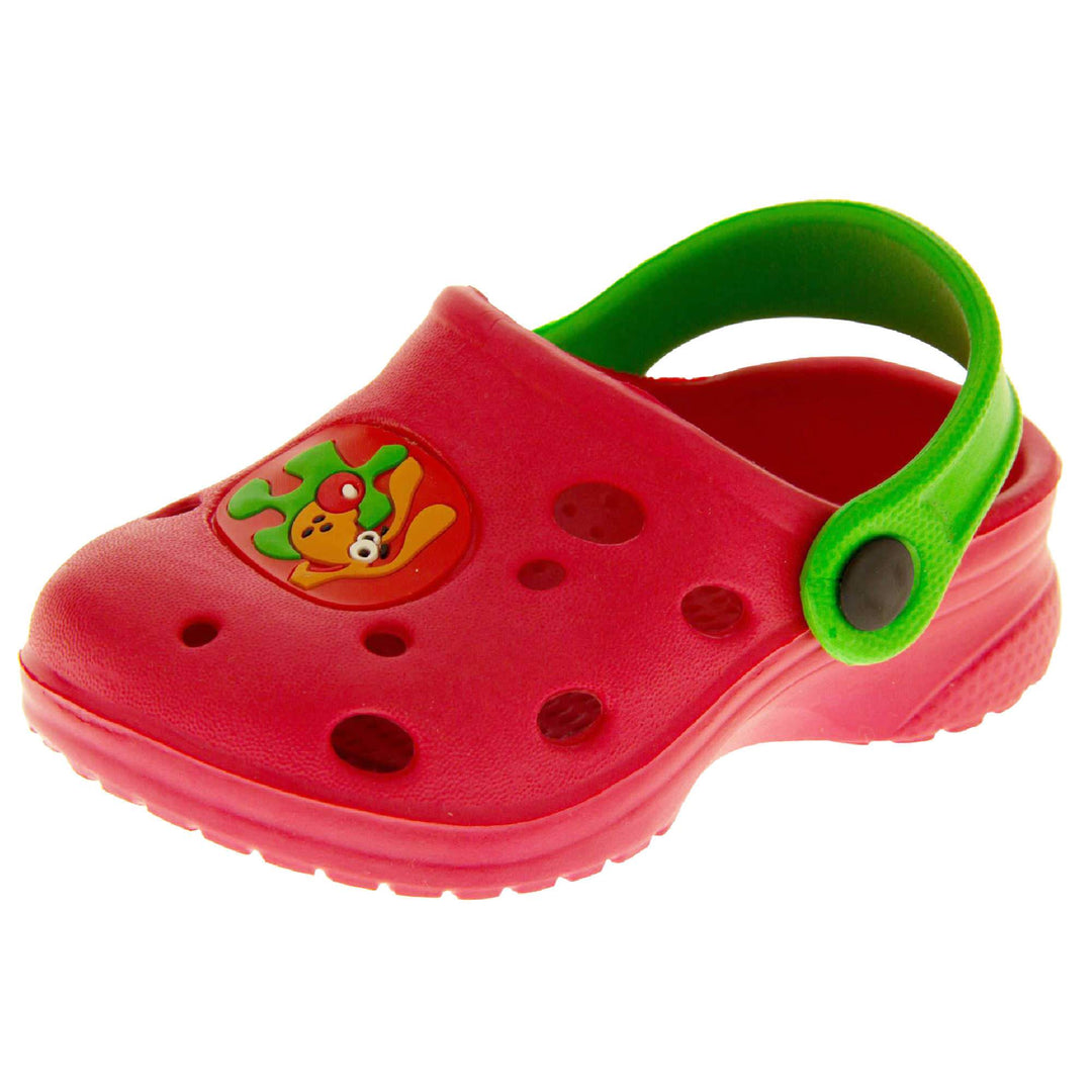Kids Summer Clogs. Red synthetic clog style shoes. Cut out holes in the upper with a cartoon dog decal in the centre centre. Green strap that goes along the back of your heel. The strap can be moved along the top of the shoe instead to make the shoe a mule. Left foot at an angle.