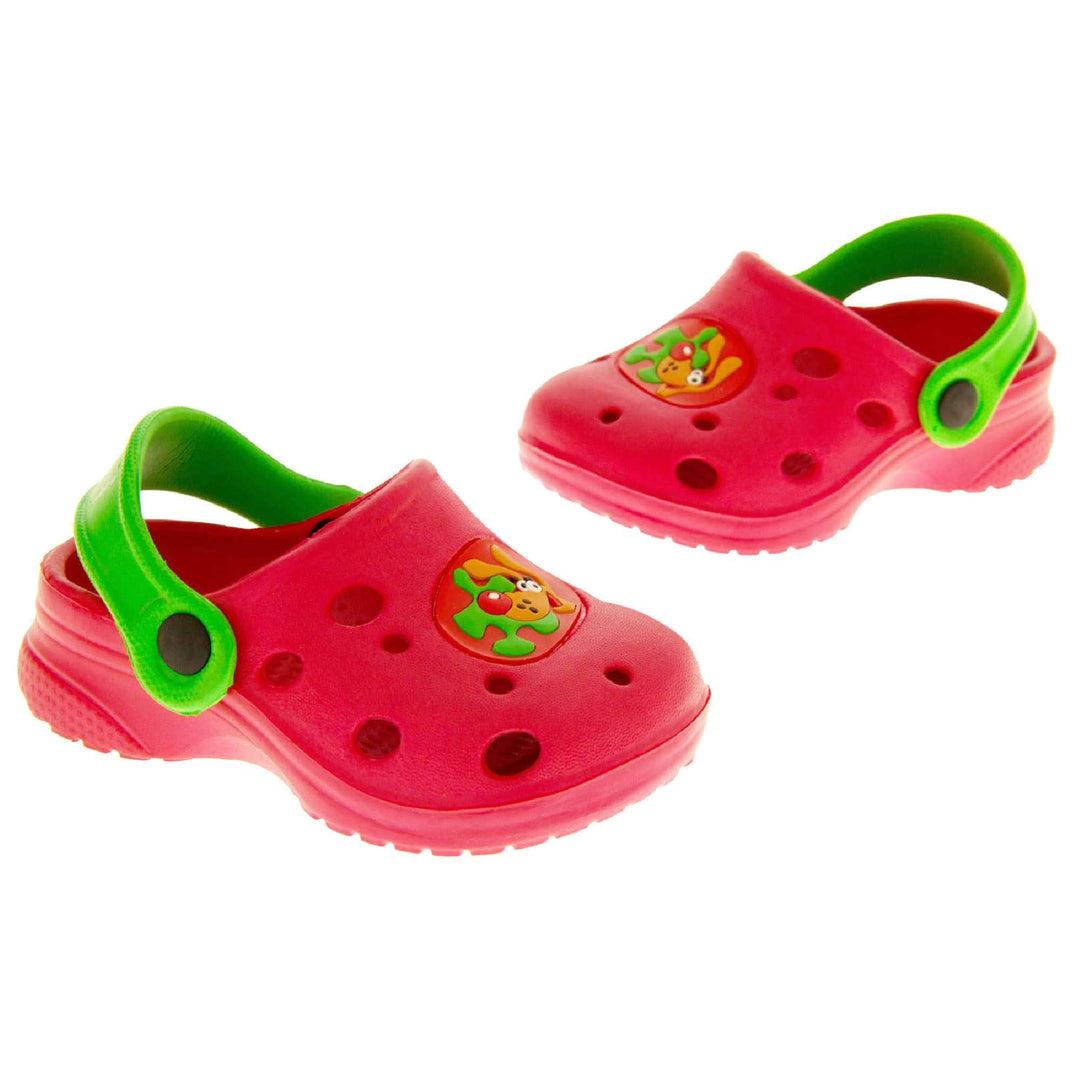 Kids Summer Clogs. Red synthetic clog style shoes. Cut out holes in the upper with a cartoon dog decal in the centre centre. Green strap that goes along the back of your heel. The strap can be moved along the top of the shoe instead to make the shoe a mule. Both feet in an L shape at a slight angle.