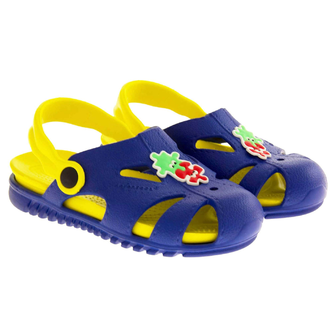 Kids pool clogs. Fisherman style synthetic sandals with blue upper and outer sole. Yellow ankle strap and insole. Green and red jigsaw pieces detail to the centre of the upper. Both shoes next to each other at a slight angle.