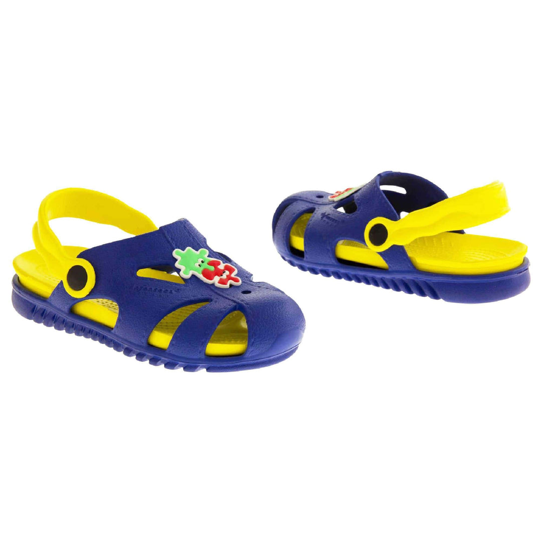 Kids pool clogs. Fisherman style synthetic sandals with blue upper and outer sole. Yellow ankle strap and insole. Green and red jigsaw pieces detail to the centre of the upper. Both shoes at a slight angle facing top to tail.