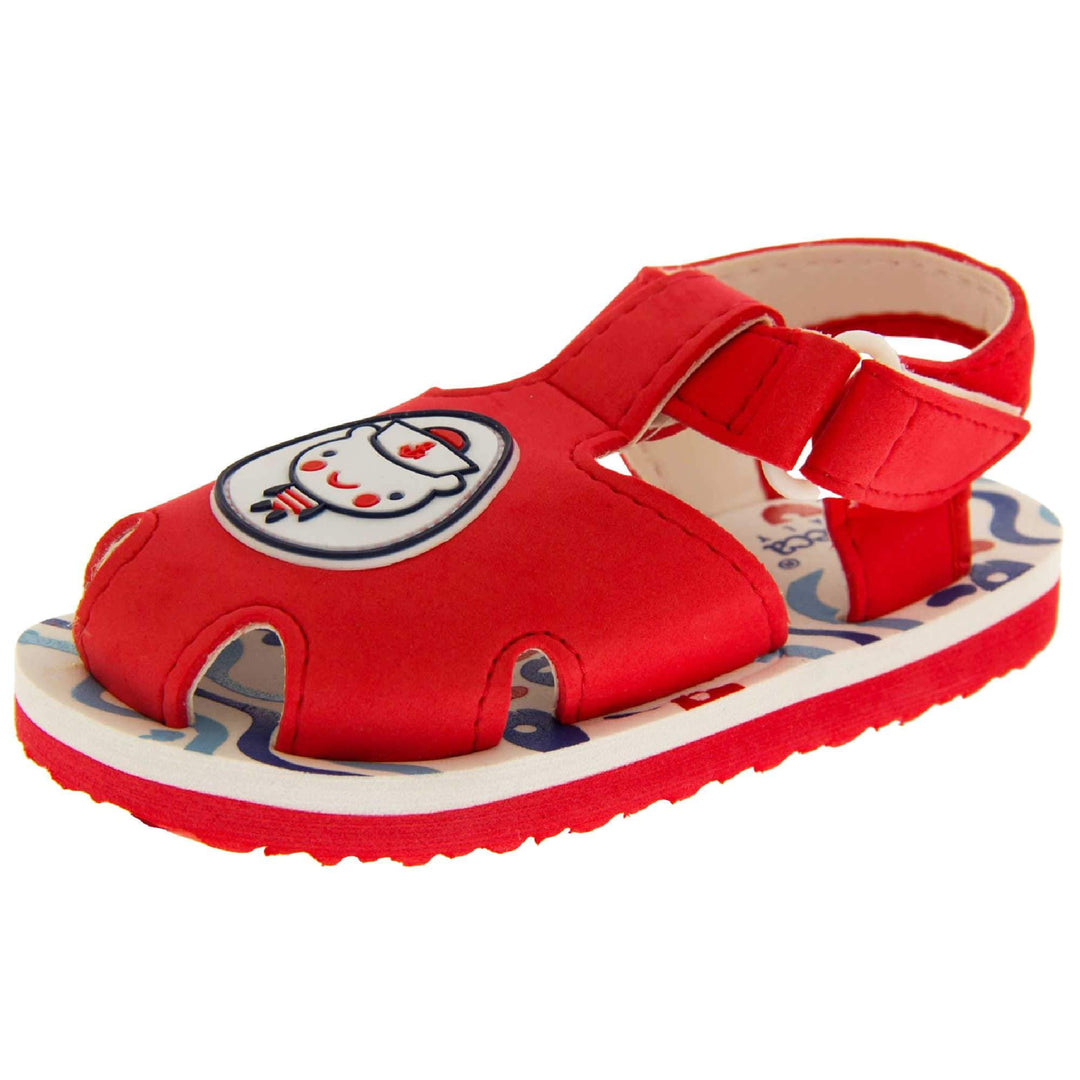 Boys Sandals. Fisherman style sandals with red upper and touch fasten ankle strap. The red upper has a white circle in the centre with a bear dressed as a sailor inside it. The inside of the upper and straps is white, as is the top half of the sole with the foot bed, which has a blue wave pattern on it. The bottom half of the sole is red and has a bumpy grip to the bottom of it. Left foot at an angle.