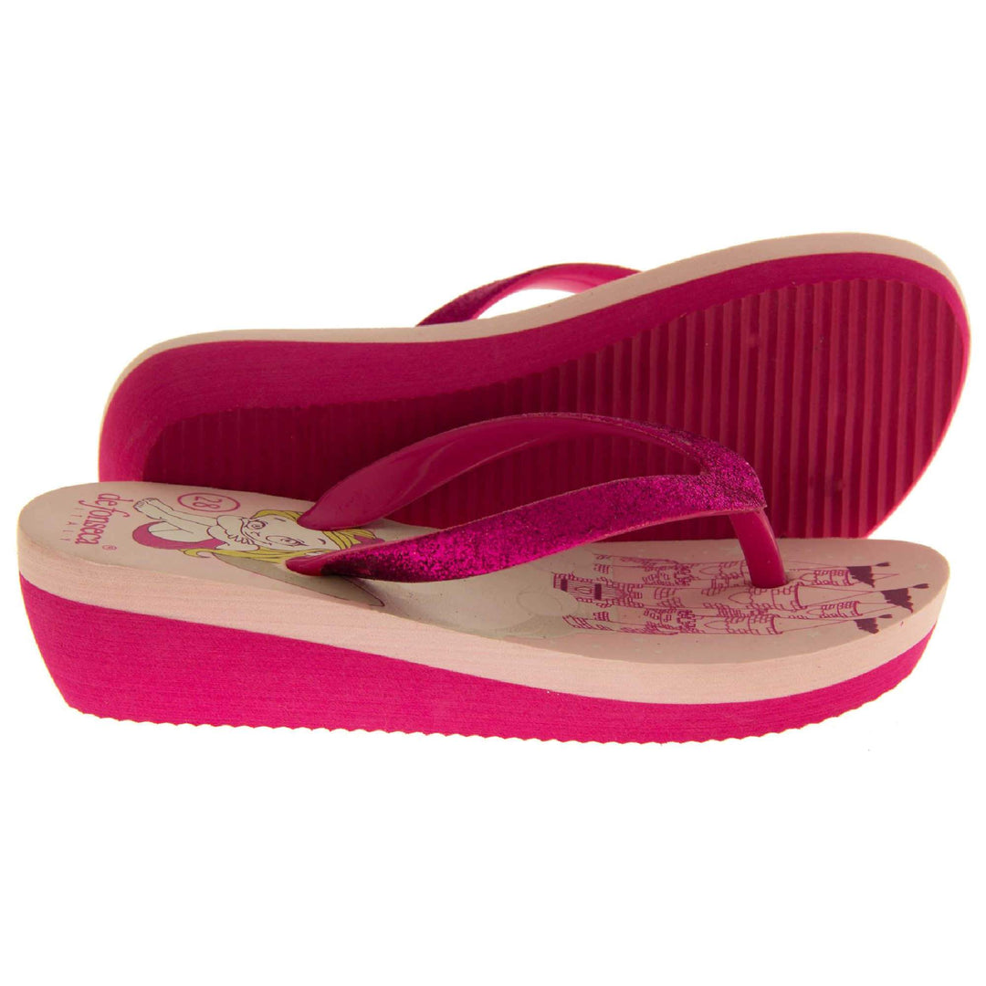 Foam wedge sandals for girls. Fuchsia bottom half of the sole with ridges for grip, baby pink top half with bright pink fantasy design to the insole. Fuchsia strap with toe post covered on top with bright pink glitter. Both feet from side profile with left foot on its side to show the sole.