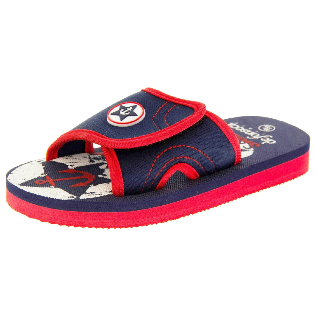 Kids sliders. Slip on slider style sandals. Navy blue touch fasten strap with red around the edge and a white synthetic circle in the centre of the strap with navy anchor in the middle. The foam sole is two toned. The top half is navy, the bottom half is red. Left foot at an angle.