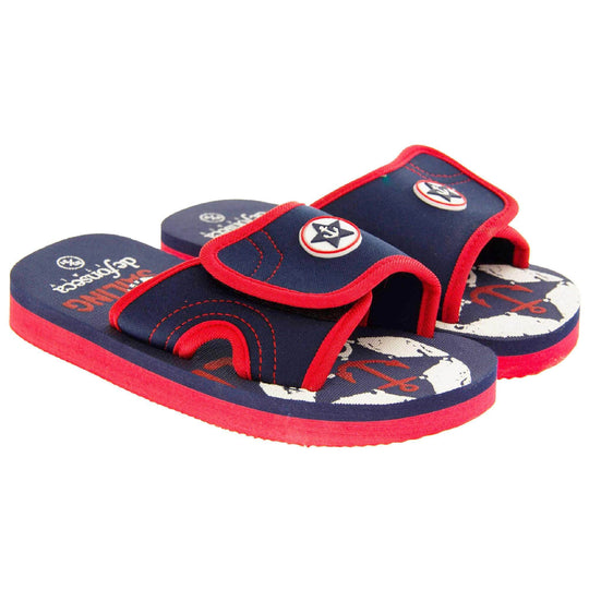 Kids sliders. Slip on slider style sandals. Navy blue touch fasten strap with red around the edge and a white synthetic circle in the centre of the strap with navy anchor in the middle. The foam sole is two toned. The top half is navy, the bottom half is red. Both shoes next to each other at a slight angle.
