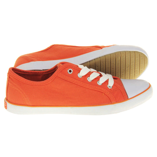 Lace up canvas sneakers. Women's shoes in a low top sneaker style with a orange canvas upper. White laces and white rubber toe bumper. Orange textile lining and white outsole with an orange line running around it and beige base. Both feet from a side profile with the left foot on its side behind the the right foot to show the sole.