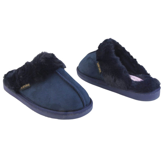 Ladies Faux Fur Mule Slippers. Slip on style slippers with Navy blue faux suede uppers. Navy faux fur lining and collar. Firm blue outsole with grip on the bottom. Both feet at an angle, facing top to tail.