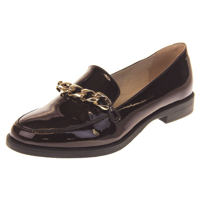 Ladies leather flat shoes. Loafer shoes in a Brogue style with a burgundy faux leather upper. Gold chain detail over the tongue. Real leather lining. Black sole with a slight heel. Left foot at an angle.