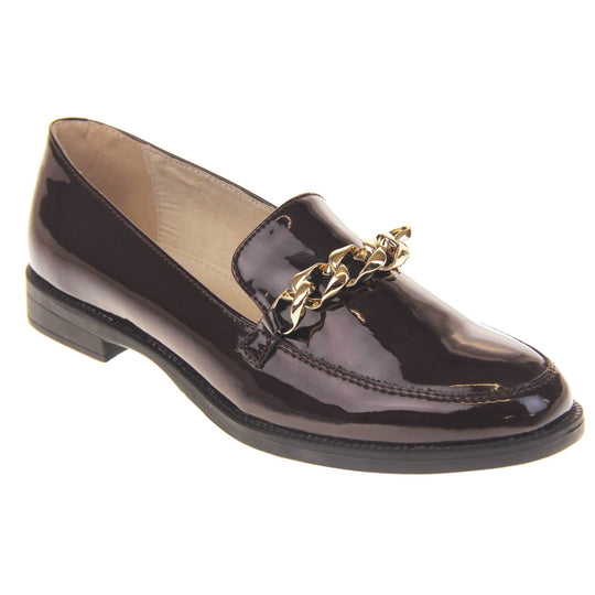 Ladies leather flat shoes. Loafer shoes in a Brogue style with a burgundy faux leather upper. Gold chain detail over the tongue. Real leather lining. Black sole with a slight heel. Right foot at an angle.