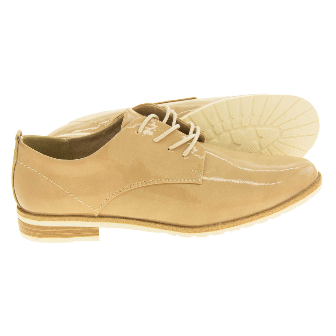 Ladies oxfords. Womens oxford style shoes with a beige patent faux leather upper. Stitching detail to the sides. Cream laces and beige lining. Brown and cream sole with a very slight heel. Both feet from a side profile with the left foot on its side behind the the right foot to show the sole.