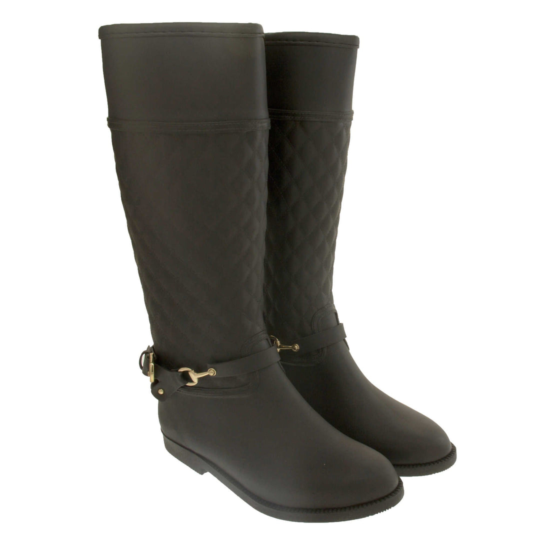 ladies wellies. Women's wellington boots in a knee length style. Black rubber upper with the leg done in a quilted effect. black rubber strap with buckle detail around the ankle. Black non slip sole. Both feet together from an angle.