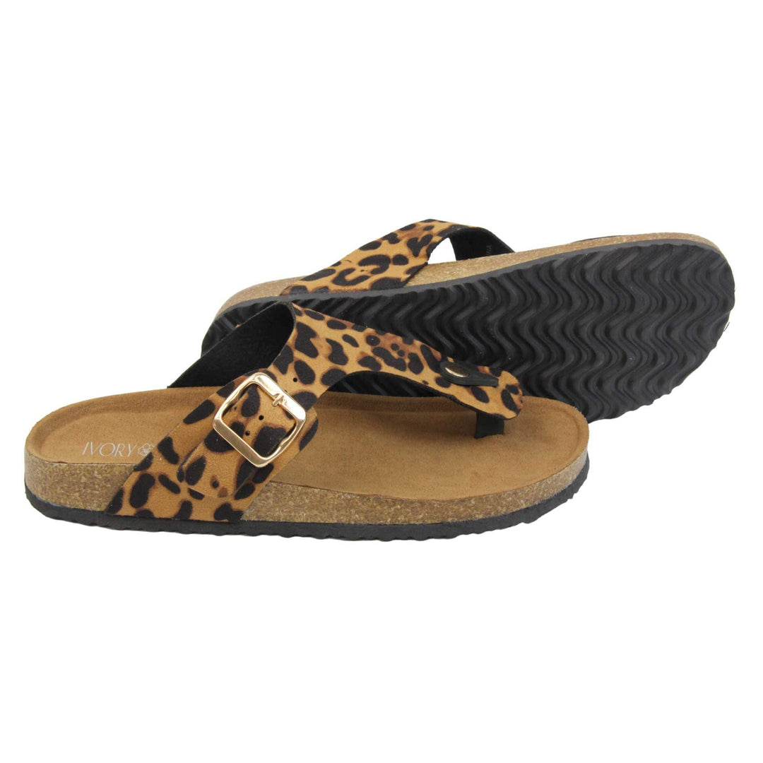 Leopard print flip flops. Leopard print faux suede strap with toe post to the front and gold buckle to the outside. Soft tan faux suede footbed with cork effect outsole and black sole. Both feet from a side profile with the left foot on its side behind the the right foot to show the sole.