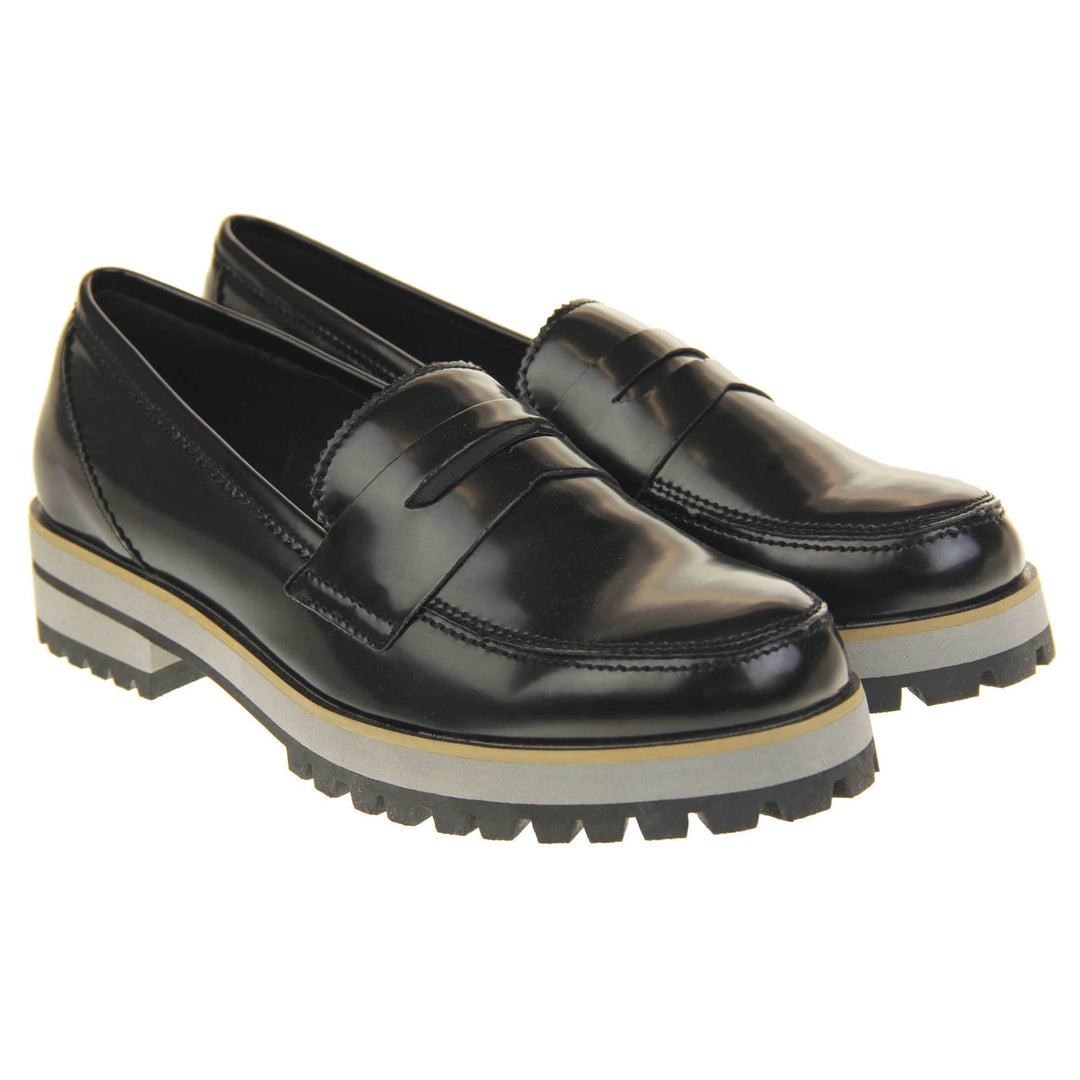 Loafer chunky sole. Loafer style shoes with a black faux leather upper. With a bar detail over the foot. Chunky black and grey sole with slip resistant grip to the bottom. Both feet together at a slight angle.