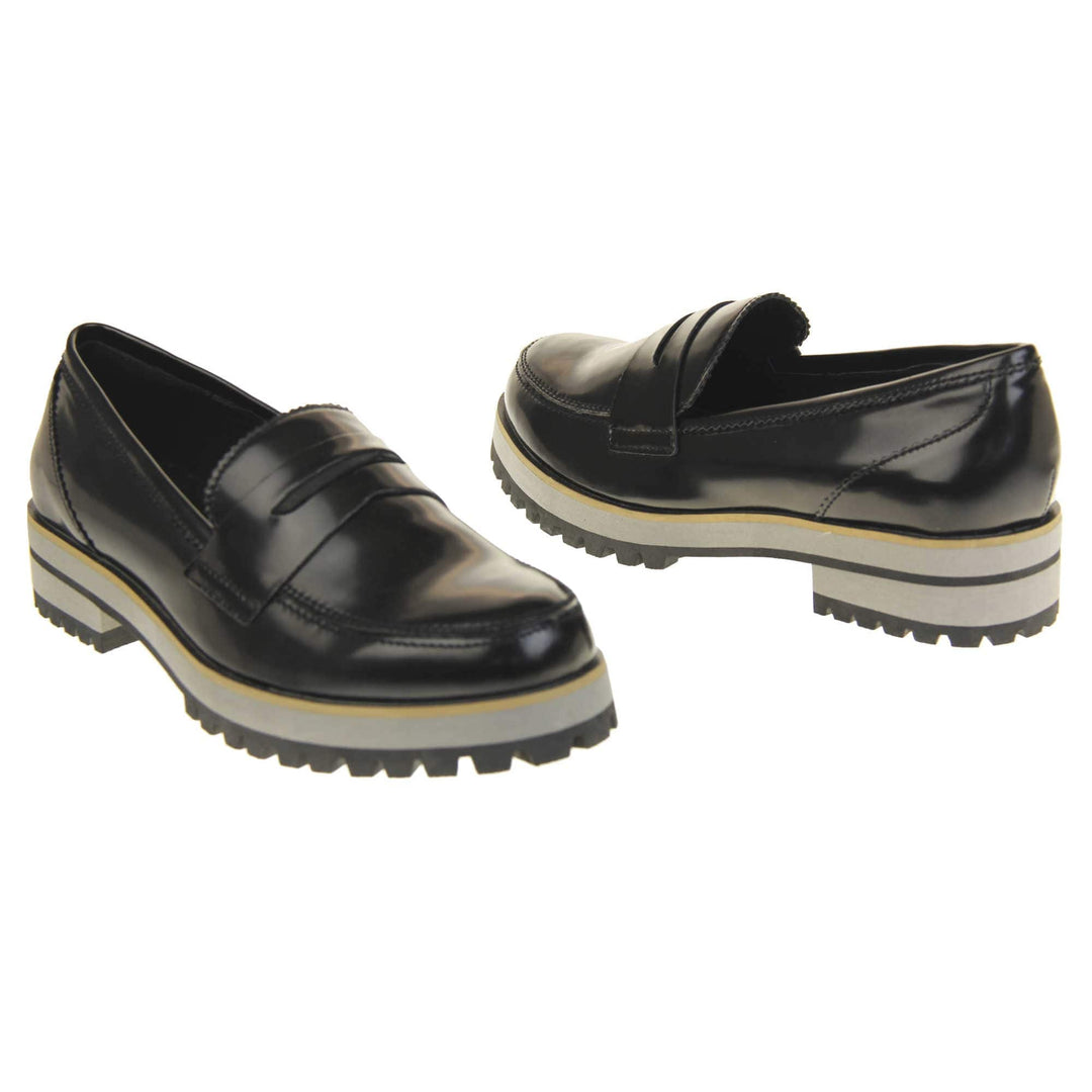 Loafer chunky sole. Loafer style shoes with a black faux leather upper. With a bar detail over the foot. Chunky black and grey sole with slip resistant grip to the bottom. Both feet at an angle facing top to tail.
