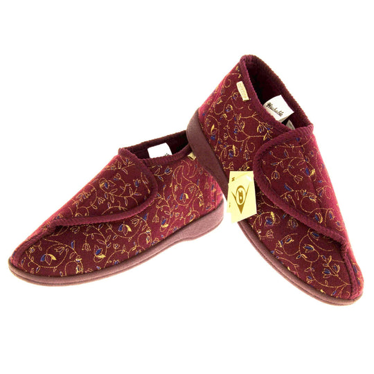 Machine washable slippers. Womens bootie style slipper with a burgundy textile upper with vine and flower embroidered design. Touch fasten tab to the top and red textile lining. Firm red sole. Both feet in a v shape with the back of the right foot lifted on top of the left.