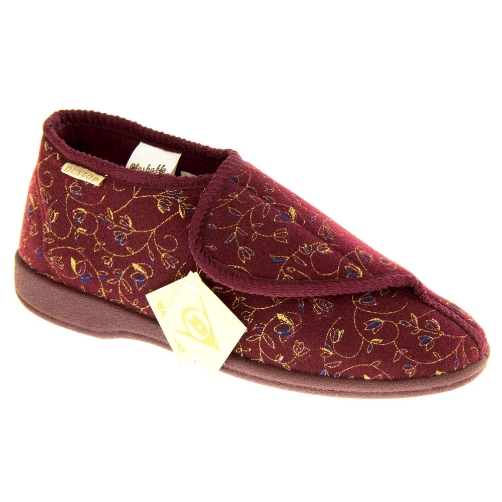 Machine washable slippers. Womens bootie style slipper with a burgundy textile upper with vine and flower embroidered design. Touch fasten tab to the top and red textile lining. Firm red sole. Right foot at an angle.