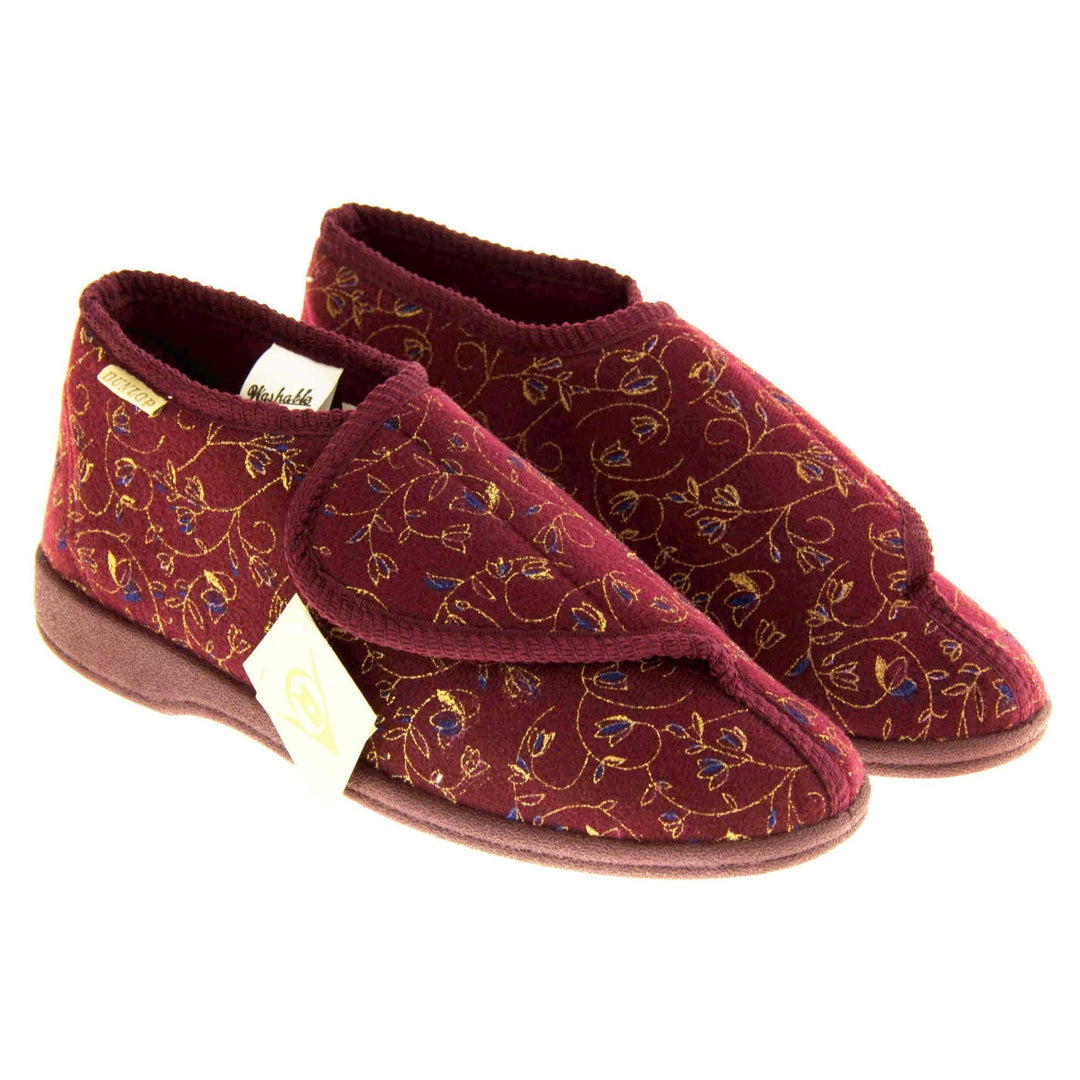 Machine washable slippers. Womens bootie style slipper with a burgundy textile upper with vine and flower embroidered design. Touch fasten tab to the top and red textile lining. Firm red sole. Both feet together at angle.