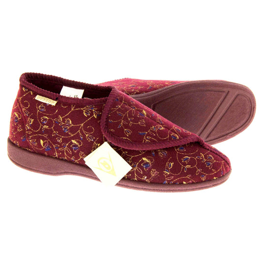 Machine washable slippers. Womens bootie style slipper with a burgundy textile upper with vine and flower embroidered design. Touch fasten tab to the top and red textile lining. Firm red sole. Both feet from a side profile with the left foot on its side behind the the right foot to show the sole.