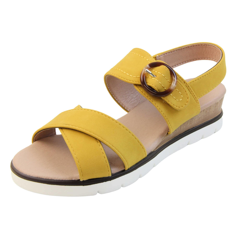 Memory foam sandal. Classic womens strappy sandals with yellow textile straps. Dual toe straps that cross over each other. The ankle strap is touch fasten but has a brown buckle detail to look like a buckle fastening. Beige faux leather memory foam insoles. Small wedge heel in cork effect. White outsole with a black rim around the top. Left foot at an angle.