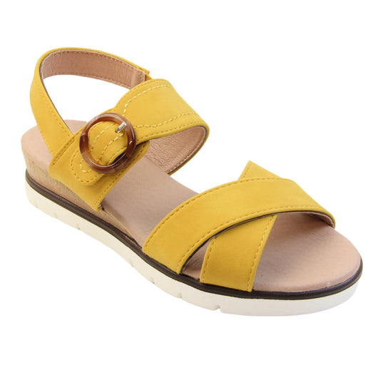 Memory foam sandal. Classic womens strappy sandals with yellow textile straps. Dual toe straps that cross over each other. The ankle strap is touch fasten but has a brown buckle detail to look like a buckle fastening. Beige faux leather memory foam insoles. Small wedge heel in cork effect. White outsole with a black rim around the top. Right foot at an angle.