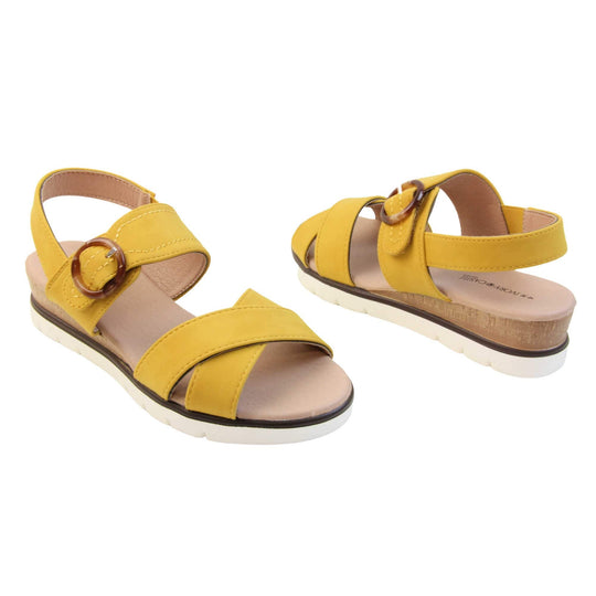 Memory foam sandal. Classic womens strappy sandals with yellow textile straps. Dual toe straps that cross over each other. The ankle strap is touch fasten but has a brown buckle detail to look like a buckle fastening. Beige faux leather memory foam insoles. Small wedge heel in cork effect. White outsole with a black rim around the top. Both shoes about an inch apart at a slight angle facing top to tail.